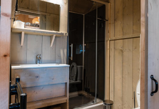 Baño en la tienda Safari Cottage Kaa en Camping Vossenberg, Países Bajos, con paredes de madera y ducha.