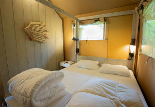 Dormitorio en Safari tent Cottage Kaa con cama doble y decoración rústica en Camping Vossenberg, Países Bajos.