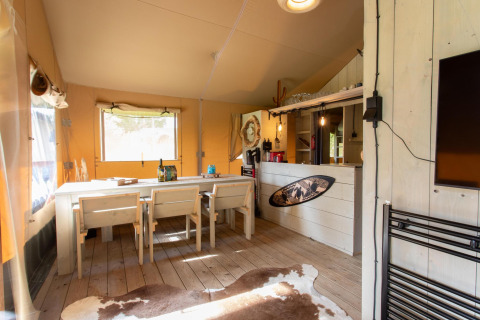 Innenraum des Safari-Zeltes Cottage Kaa auf Camping Vossenberg in den Niederlanden, mit Holztisch und Stühlen.