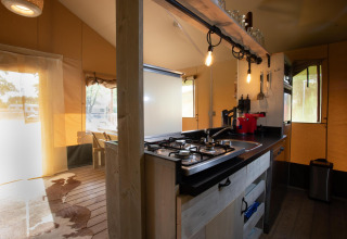 Cocina dentro de la Safari tent Cottage Kaa en Camping Vossenberg, Países Bajos, con estufa y decoración moderna.