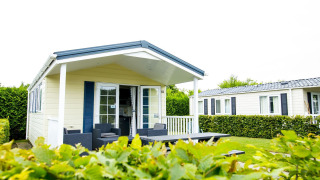 Delta Lodge bij Holiday Park Duinhoeve in Nederland met terras, tuinmeubilair en groene heggen.