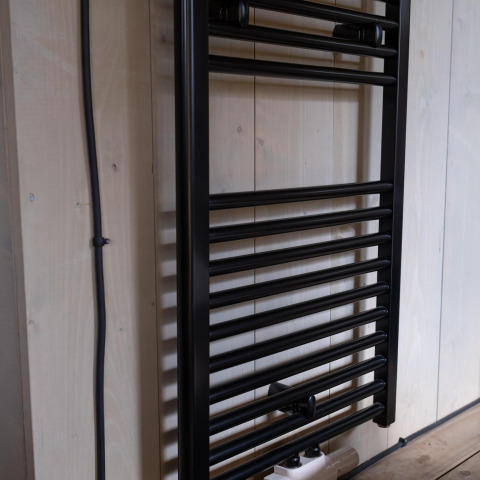 Zwarte handdoekradiator aan houten wand in Safari tent Cottage Kaa bij Camping Vossenberg, Nederland.