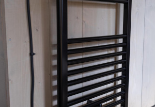 Black towel radiator mounted on a wooden wall in Safari tent Cottage Kaa at Camping Vossenberg, Netherlands.