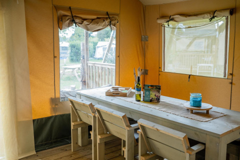 Interior de la Safari tent Cottage Kaa en Camping Vossenberg, Países Bajos, con mesa y sillas rústicas.