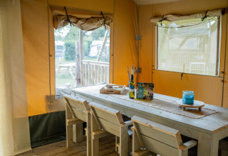 Interior de la Safari tent Cottage Kaa en Camping Vossenberg, Países Bajos, con mesa y sillas rústicas.