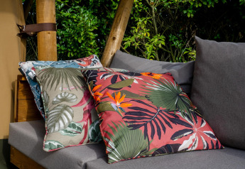 Decorative pillows with tropical leaf prints on a gray sofa at Safari tent Cottage Kaa, Camping Vossenberg.