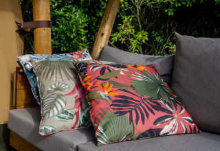 Cojines decorativos con estampado tropical en un sofá gris del Safari tent Cottage Kaa en Camping Vossenberg, Holanda.