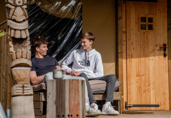 To unge mænd slapper af og taler foran Safari tent Cottage Kaa på Camping Vossenberg i Holland.