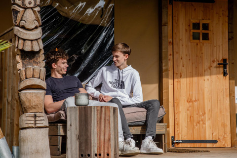 Zwei junge Männer entspannen sich und unterhalten sich vor dem Safari-Zelt Cottage Kaa in den Niederlanden.