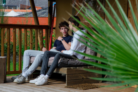 Two young men chatting on the porch of Safari tent Cottage Kaa at Camping Vossenberg in the Netherlands.