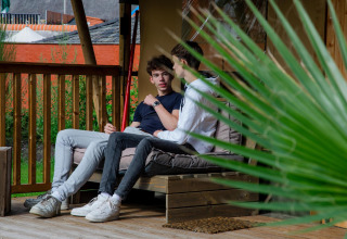 Deux jeunes hommes discutent sur la terrasse de la Safari tent Cottage Kaa au Camping Vossenberg, aux Pays-Bas.