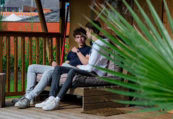 Two young men chatting on the porch of Safari tent Cottage Kaa at Camping Vossenberg in the Netherlands.