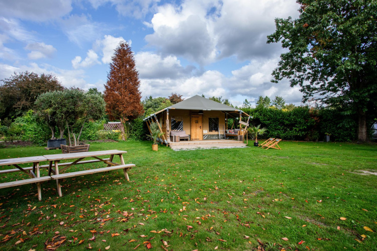 Tienda Safari Cottage Kaa en Camping Vossenberg, Países Bajos, rodeada de árboles y césped verde amplio.