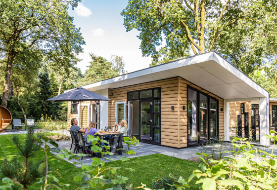 Moderne Silva sauna lodge in groene omgeving met gezin dat buiten eet onder een grote parasol.