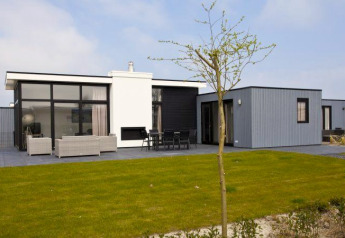 Moderne L-Cube 6 lodge ved Schoneveld i Holland, med glasfacade, terrasse og grøn græsplæne foran.