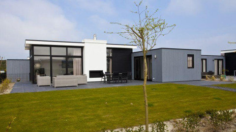 Moderne L-Cube 6 lodge bij Schoneveld in Nederland, met glasgevel, terras en een groene grasmat.