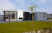 Moderne L-Cube 6 lodge ved Schoneveld i Holland, med glasfacade, terrasse og grøn græsplæne foran.
