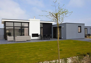 Modernes L-Cube 6 Lodge in Schoneveld, Niederlande, mit Glasfront, Terrasse und Rasen davor.