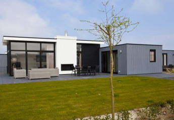 Modernes L-Cube 6 Lodge in Schoneveld, Niederlande, mit Glasfront, Terrasse und Rasen davor.