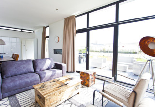 Sala moderna en L-Cube 6 en Schoneveld, Países Bajos, con grandes ventanales y muebles contemporáneos.