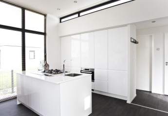 Moderne, minimalistische keuken in L-Cube 6 op Schoneveld, Nederland, met witte kasten en grote ramen.