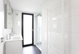 Salle de bain moderne du L-Cube 6 à Schoneveld, Pays-Bas, avec douche, porte vitrée et sèche-serviettes.