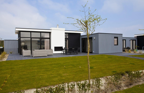 Moderne lodge L-Cube 6 bij Schoneveld in Nederland, met groot terras, gazon en stijlvol exterieur.