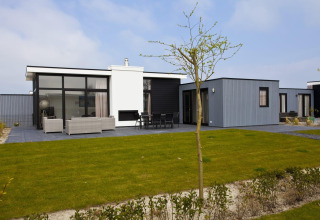 Moderne lodge L-Cube 6 bij Schoneveld in Nederland, met een ruim terras, grasveld en stijlvol uiterlijk.