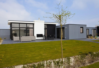 Moderne lodge L-Cube 6 bij Schoneveld in Nederland, met groot terras, gazon en stijlvol exterieur.