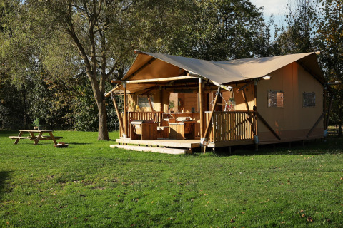 Glamping tent La Vida op Resort de Parel, Nederland, met houten terras en picknickbank op een grasveld.