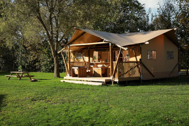 Glamping tent La Vida at Resort de Parel, Netherlands, with wooden porch and picnic table in grassy setting.