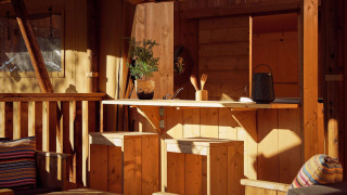 Coin cuisine d’une tente safari avec mobilier en bois, plantes en pot, coussins et lumière du soleil.