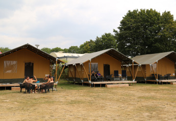 Safari-telte ved Rhederlaagse Meren i Holland, folk slapper af udenfor med borde og stole på græsset.