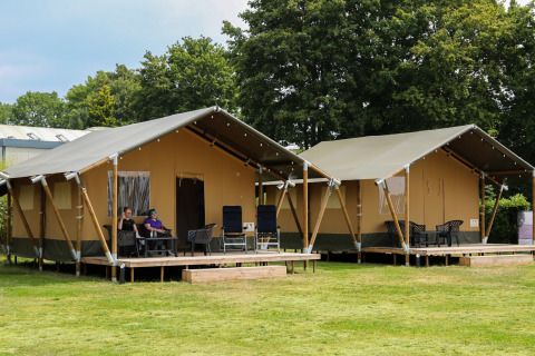 Twee safaritenten met veranda aan recreatiepark Rhederlaagse Meren, Nederland, met relaxerende mensen.