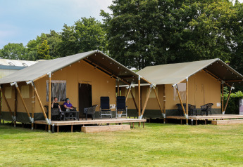 Twee safaritenten met veranda bij Recreatiepark Rhederlaagse Meren, Nederland, met mensen die ontspannen.