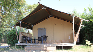 Safari-Zelt mit überdachter Terrasse und Kunststoffmöbeln im Rhederlaagse Meren, Niederlande, von Bäumen umgeben.