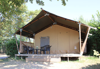 Safari-Zelt mit überdachter Terrasse und Kunststoffmöbeln im Rhederlaagse Meren, Niederlande, von Bäumen umgeben.
