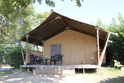Safari tent with covered porch and plastic furniture at Rhederlaagse Meren, Netherlands, surrounded by trees.