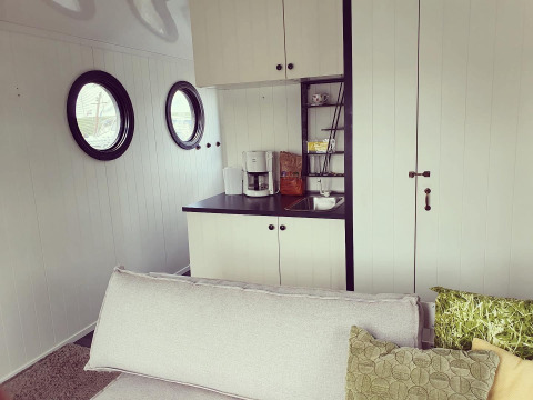 Gezellige woonkamer en kitchenette op woonboot aan Rhederlaagse Meren, Nederland, met ronde ramen.