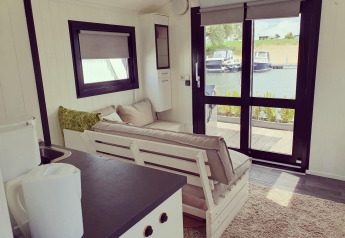 Interno di una houseboat al Rhederlaagse Meren, Paesi Bassi, con vista sul porto turistico dalle vetrate.