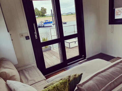 Blick aus dem Wohnzimmer eines Hausboots im Erholungspark Rhederlaagse Meren mit Sofa und Seeblick.