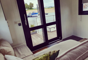 Vue depuis le salon d'une péniche au parc de loisirs et marina Rhederlaagse Meren, avec canapé et vue sur l'eau.