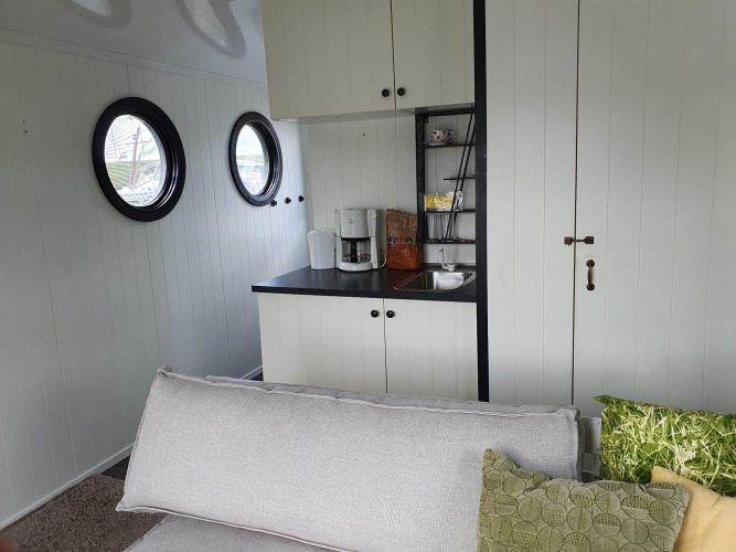 Lichte woonkamer met keukenhoek, bank, patrijspoorten en koffiezetapparaat in een houseboat bij Rhederlaagse Meren.