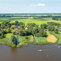 Vista aerea di un parco vacanze con sistemazioni glamping, circondato da campi verdi, alberi e un fiume.