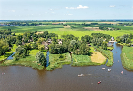 Vista aérea de un parque vacacional con alojamientos glamping, rodeado de campos verdes, árboles y un río.