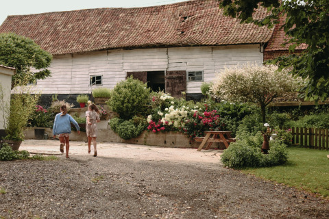 Deux enfants courent devant une grange rustique et un jardin à Feather Down Fermette des trois tilleuls, Hauts-de-France.