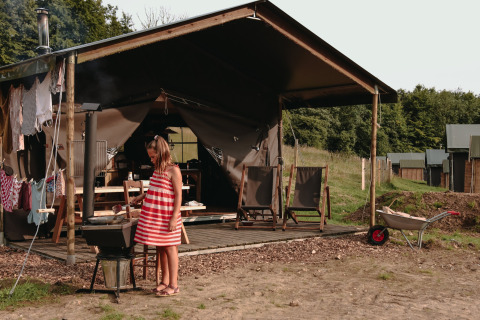 Bambina con vestito a righe rosse davanti a una tenda a Fermette des trois tilleuls, Hauts-de-France.