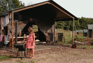 Bambina con vestito a righe rosse davanti a una tenda a Fermette des trois tilleuls, Hauts-de-France.