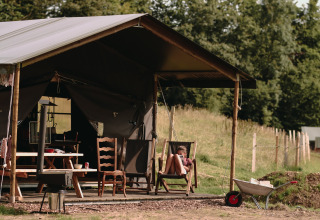 A person relaxes in a chair on a porch outside a tent at Feather Down Fermette des trois tilleuls in France.