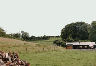 Landskabsbillede nær Bezinghem i Hauts-de-France med en lade, grønne marker og skov i baggrunden.